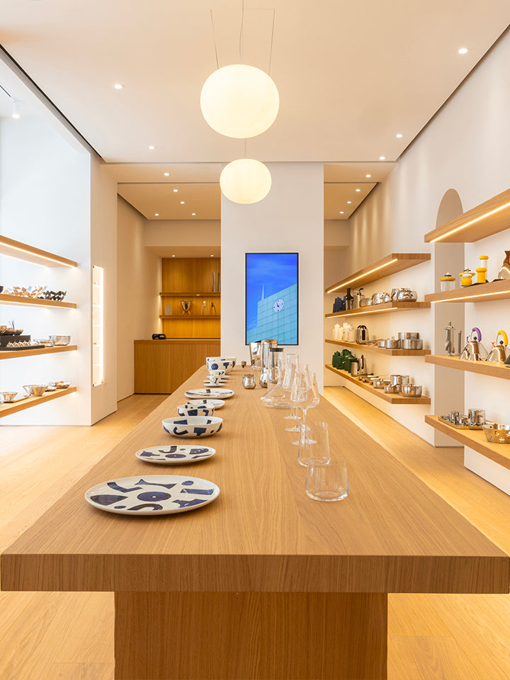 Minimalist Alessi store interior with warm wood shelves, glowing pendant lights, and elegant tableware on display.