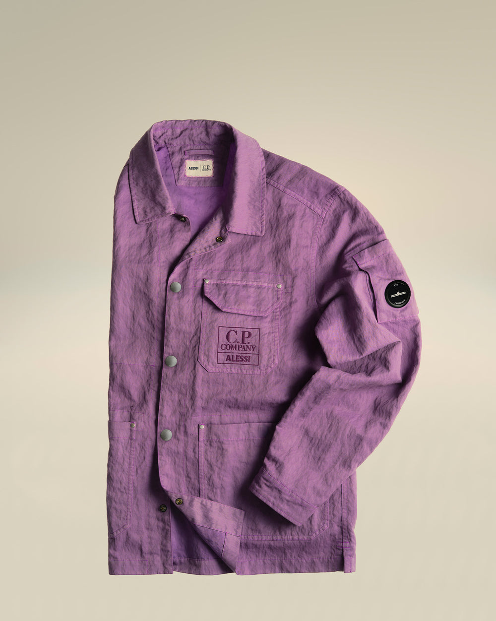 Purple textured jacket by Alessi with C.P. Company lens badge, front logo, buttons, and multiple pockets, laid flat.