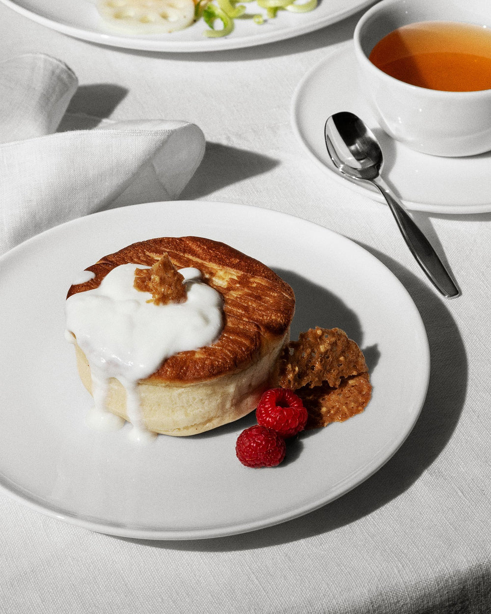 White ceramic Itsumo table set by Alessi, featuring a round plate, cup, saucer, and linen napkin on a white tablecloth.