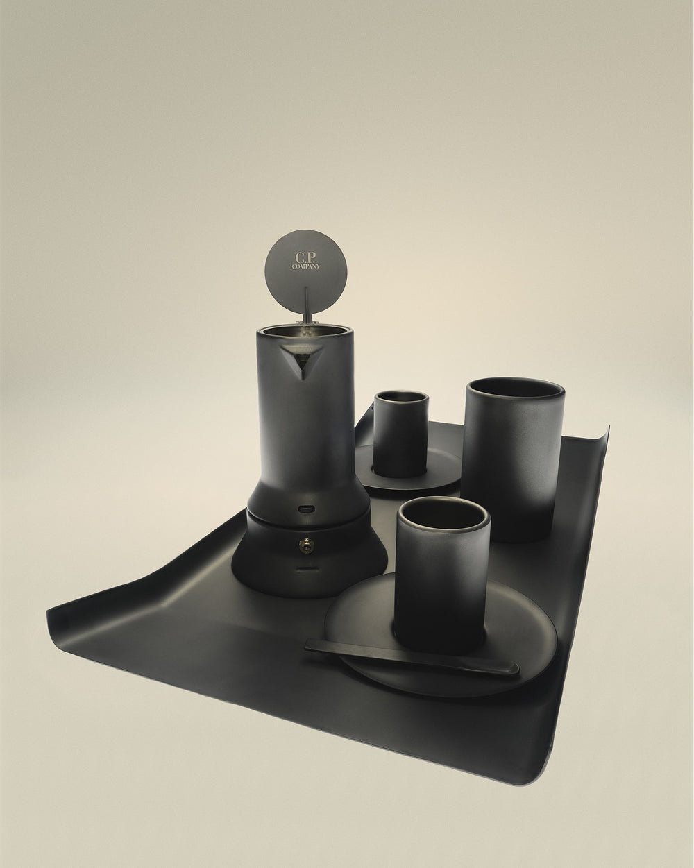 Matte black Arran tray by Alessi, featuring a unique curved edge, holding a dark coffee maker and three cups with saucers.