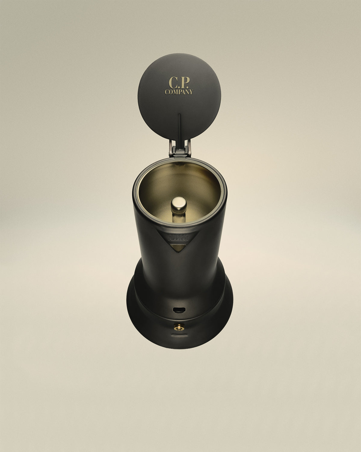 Dark grey espresso coffee maker by Alessi with lid open, revealing gold interior and 'C.P. COMPANY' text.