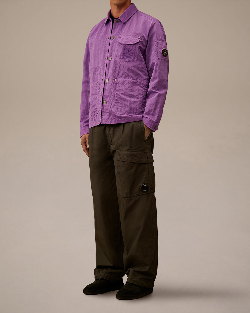 Purple jacket by Alessi with embroidered 'C.P. COMPANY' chest pocket and lens badge on sleeve, styled with dark cargo pants.