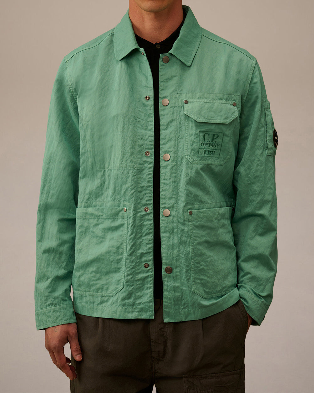 Mint green crinkled utility jacket by Alessi, featuring snap buttons, utility pockets, embroidered C.P. Company logo, and sleeve badge.