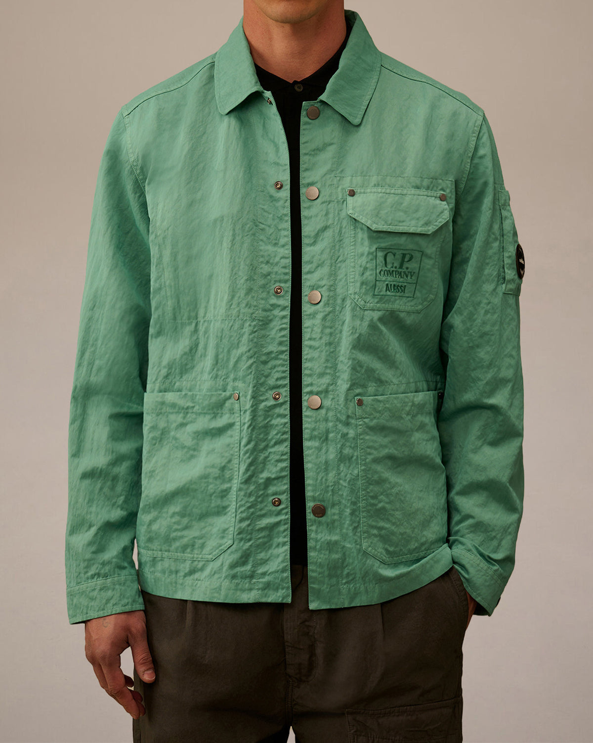 Mint green crinkled utility jacket by Alessi, featuring snap buttons, utility pockets, embroidered C.P. Company logo, and sleeve badge.