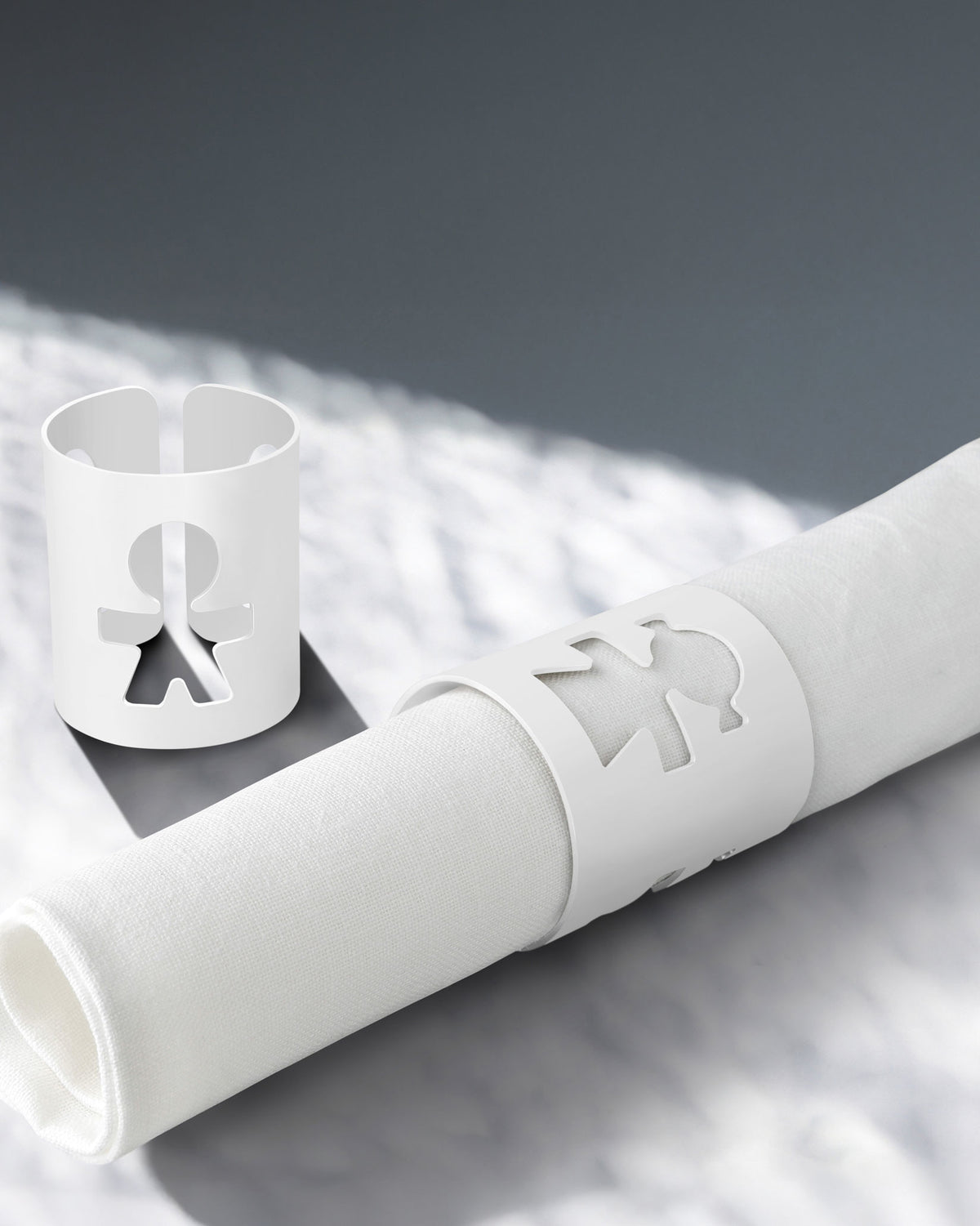 White napkin holders by Alessi with a human figure cut-out design, one holding a rolled white napkin.