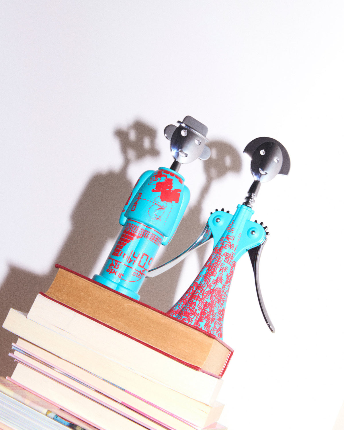 Turquoise Anna G. corkscrew by Alessi with red patterns, standing with a male-figure corkscrew on a stack of books.