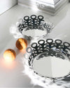 Silver metallic fruit holder by Alessi with abstract cutout design, next to another and two oranges on a white table.