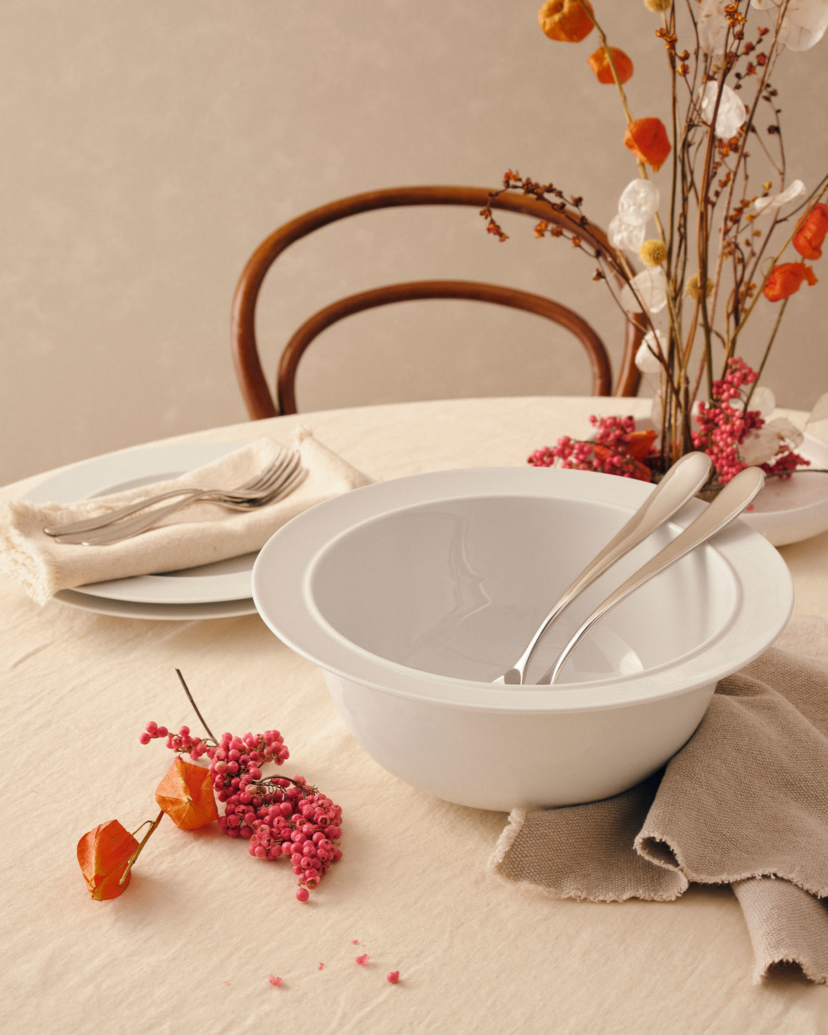 White ceramic salad serving bowl by Alessi, holding two serving forks, styled on a table with dried flowers and pink berries.