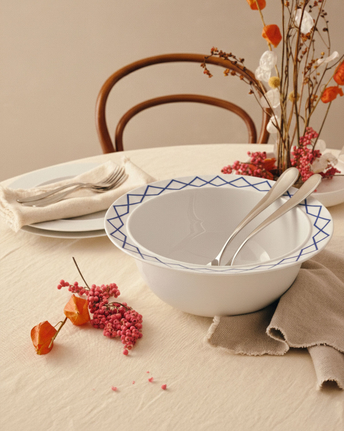 White ceramic salad serving bowls by Alessi with blue geometric diamond pattern rims, nested with two silver serving utensils.