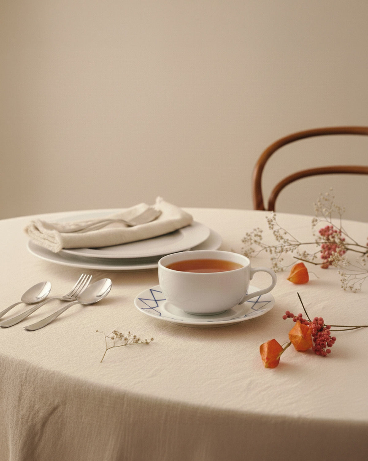 White ceramic saucer by Alessi with blue geometric patterns, holding a teacup on a beige tablecloth with flowers.