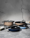 Various non-stick beige and blue pots and pans by Alessi displayed on a grey countertop.