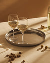 Silver round tray by Alessi with a dimpled concentric circle pattern, holding two wine glasses.