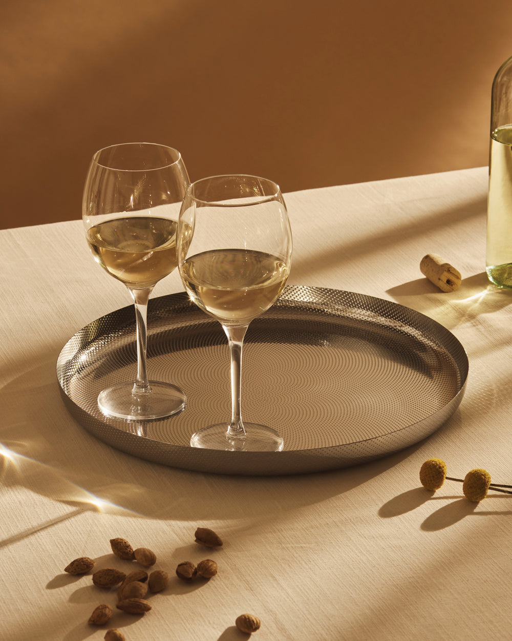 Silver round tray by Alessi with a dimpled concentric circle pattern, holding two wine glasses.