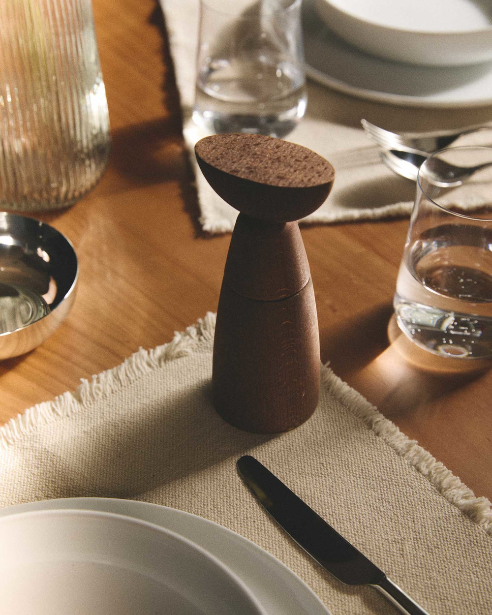 Dark wood conical spice grinder by Alessi with a flat, textured cork top on a dining table setting.