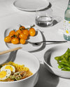 White serving plates by Alessi arranged on a table with yellow tomatoes and green edamame.