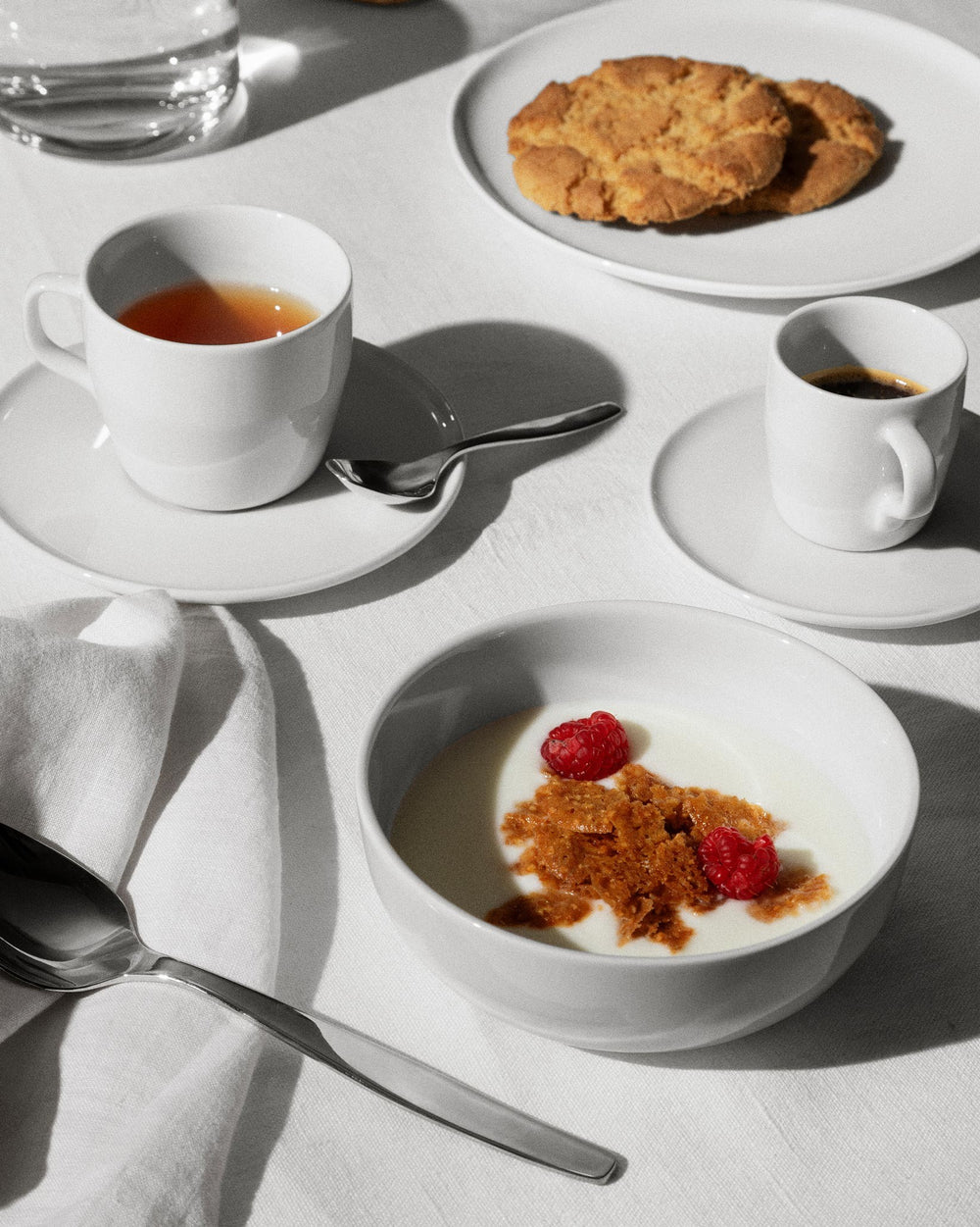 White small bowl by Alessi, filled with yogurt, granola, and fresh raspberries, amidst a breakfast setting.
