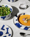 White ceramic dinnerware set by Alessi featuring bold blue abstract patterns, presented with food.
