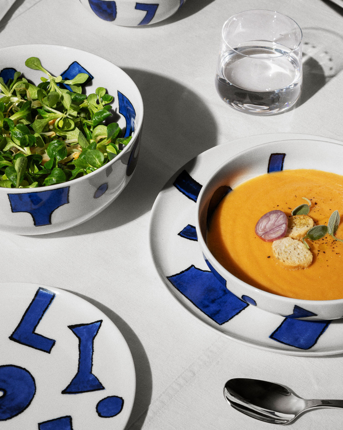 White ceramic dinnerware set by Alessi featuring bold blue abstract patterns, presented with food.