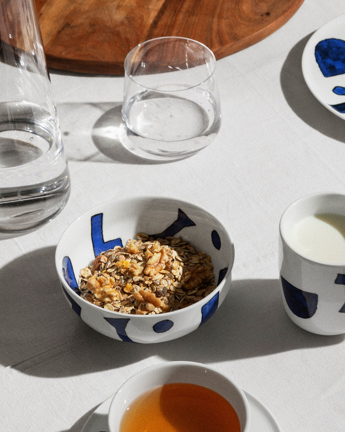 White ceramic Itsumo Yunoki table set by Alessi, with blue abstract patterns, presented in a breakfast setting.