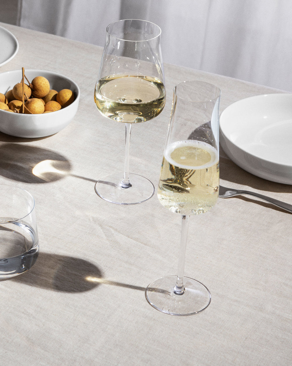 Clear glass champagne flute by Alessi, filled with sparkling wine on a light linen table setting.