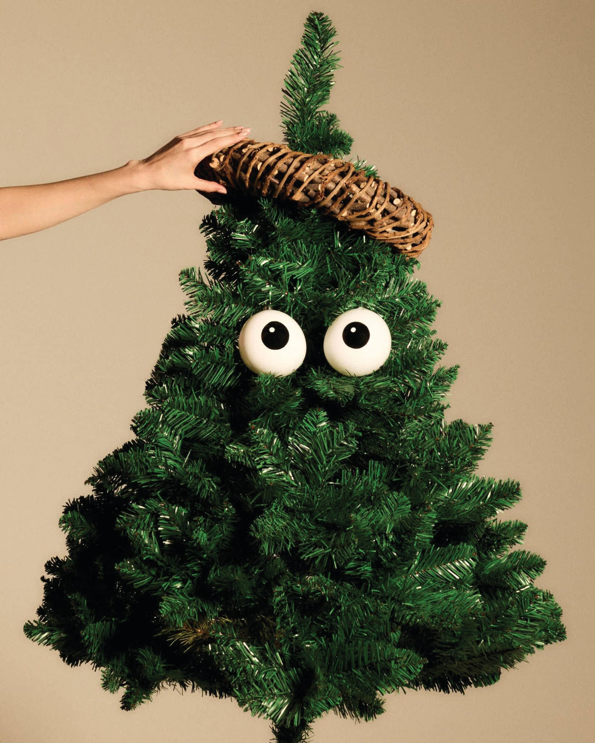 White googly eyes and woven ring Christmas tree ornaments by Alessi, on a green artificial tree, a hand adjusting the top.