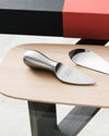 Sleek, brushed stainless steel cheese server by Alessi, engraved with '50 IL CONSORZIO 1954~2004 ANNI', on a light wood board.