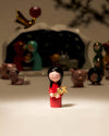Red figurine by Alessi with black hair holding a golden star, in a stylized nativity scene.