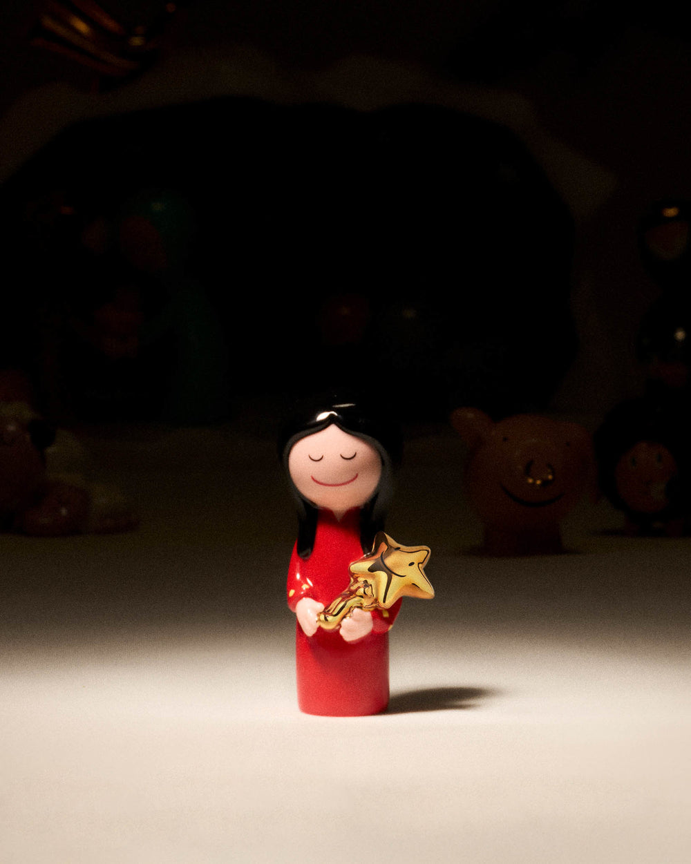 Red girl ornamental figurine by Alessi, with black hair and a gentle smile, holding a shiny gold star.