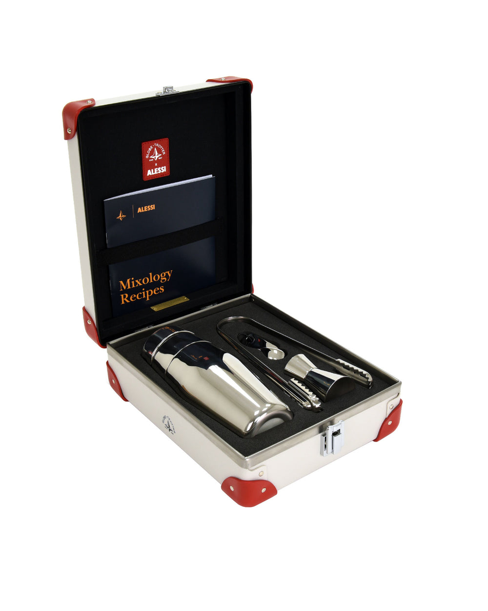 Silver cocktail shaker by Alessi, in an open white case with red corners, accompanied by jigger, tongs, and a recipe book.