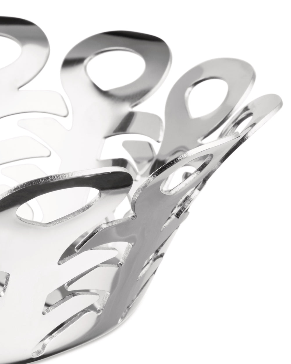 Silver perforated metal fruit holder by Alessi with an intricate, flowing cut-out design and a highly reflective surface, angled close-up.