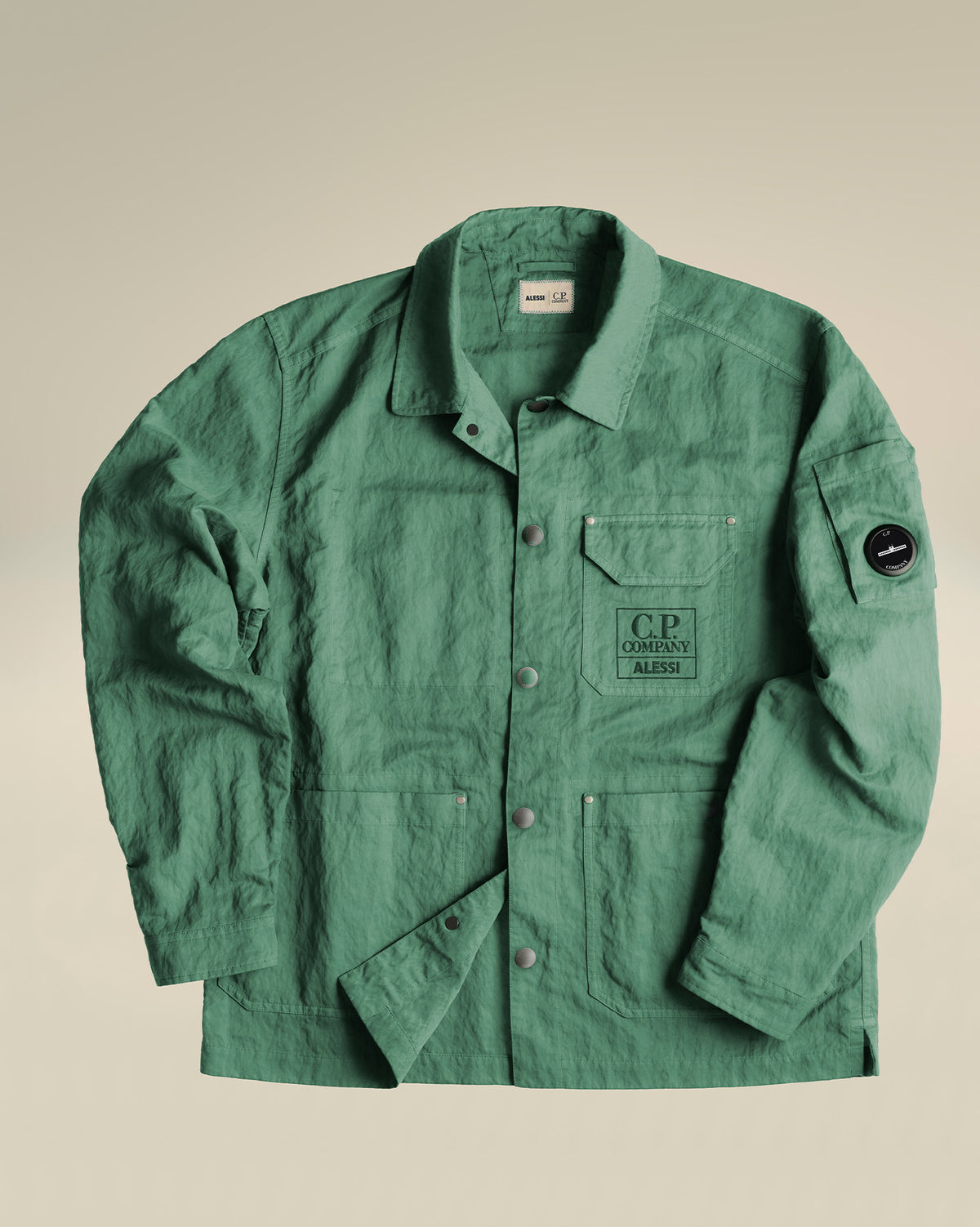Dark green crinkled utility jacket by Alessi, with 'C.P. Company ALESSI' chest print, sleeve lens, and snap buttons.