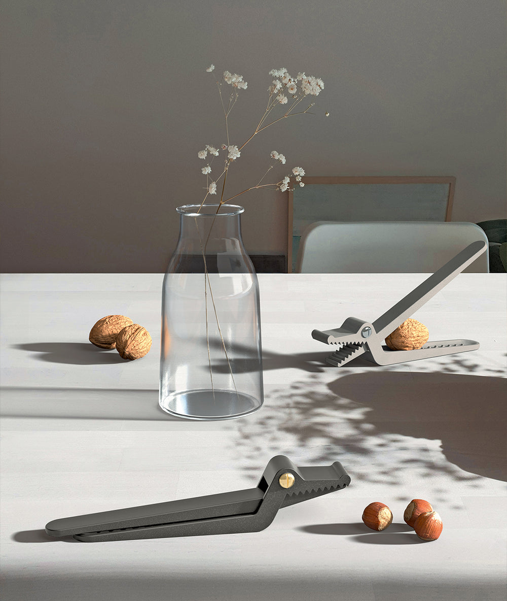 Dark gray alligator-shaped metal nutcracker by Alessi, shown open with a walnut and closed, on a white table.