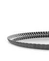 Dark grey metallic tray by Alessi with a distinctive pleated wavy rim, shown from a low angle.