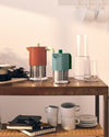 Two terracotta and teal espresso coffee makers by Alessi with ribbed stainless steel bases, on a wooden shelf.
