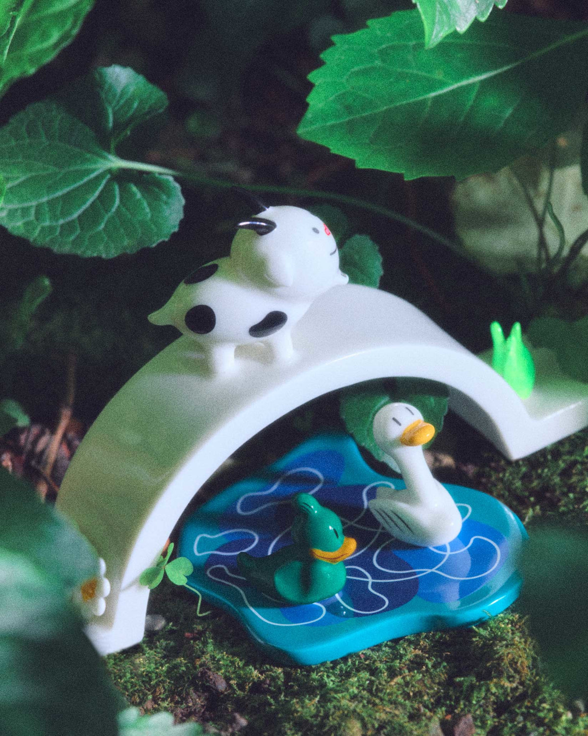 White spotted ornamental figurine by Alessi, standing on a white bridge above a blue pond with two duck figures.
