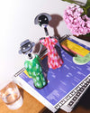 Pink and red patterned Anna G. corkscrew by Alessi, a stylized female figure, standing with a green corkscrew.