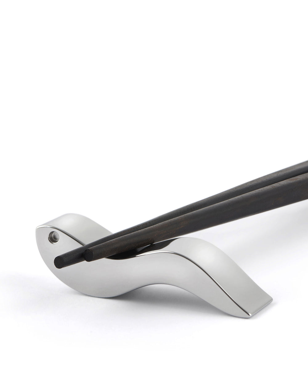 Dark wooden chopsticks by Alessi, resting on a sleek silver metallic holder.