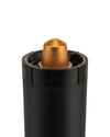 Black cylindrical capsule crusher by Alessi with a golden ribbed coffee capsule inserted at the top.