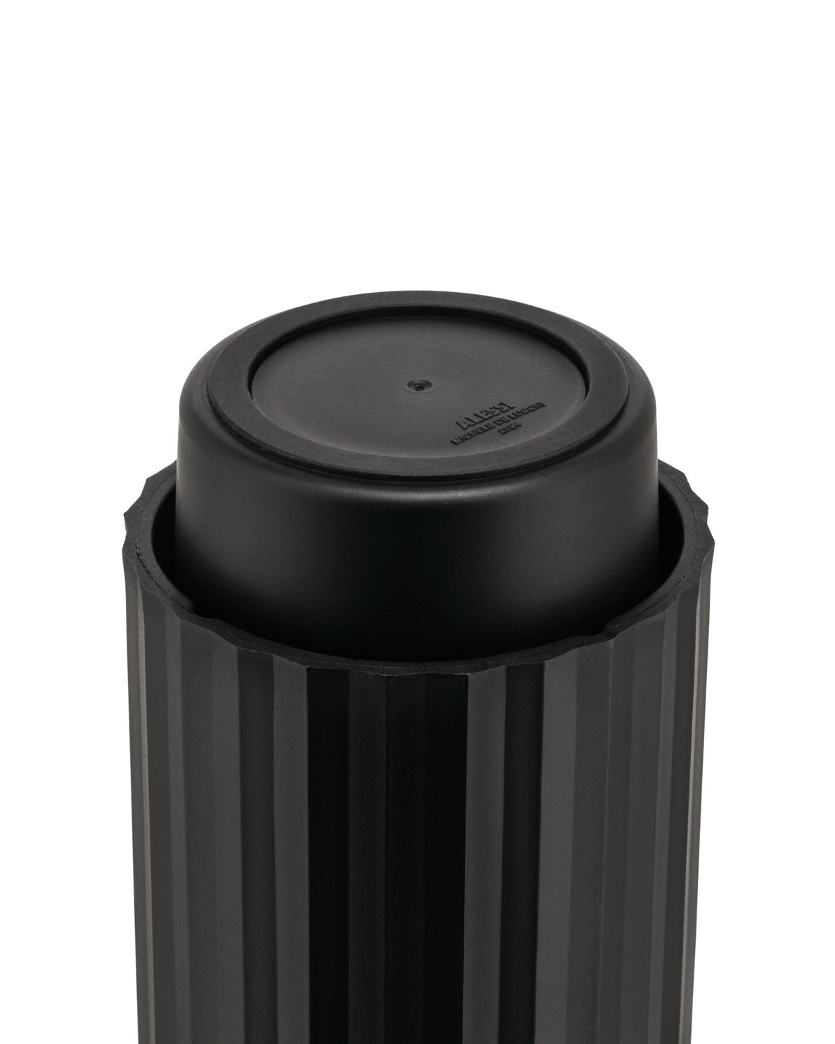 Black capsule crusher by Alessi, with a ribbed outer casing and embossed text on its smooth inner top surface.