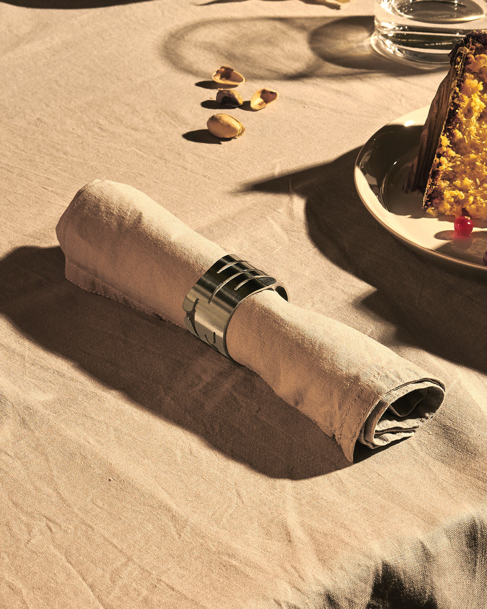 Brushed silver metal napkin holder by Alessi featuring a laser-cut bark-like pattern, holding a beige linen napkin.