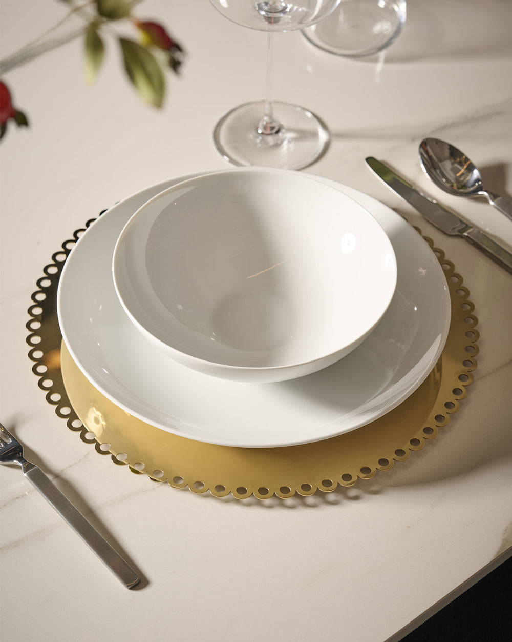 Gold scalloped tray by Alessi, holding white stacked dishes on a white marble table with cutlery.