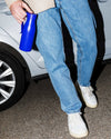 Bright blue thermo insulated bottle by Alessi with a handle and push-button lid, held by a person in jeans.