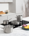 Brushed stainless steel lids by Alessi with minimalist square handles, placed on various pots in a modern kitchen.