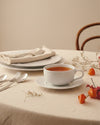 White round saucer by Alessi on a textured beige tablecloth, surrounded by fall-themed decor.