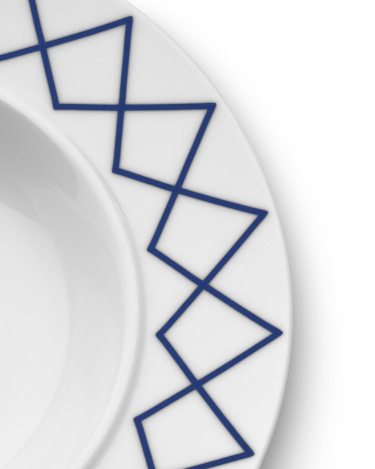 White soup bowl by Alessi with a dark blue geometric zigzag pattern on the rim, in a cropped view.