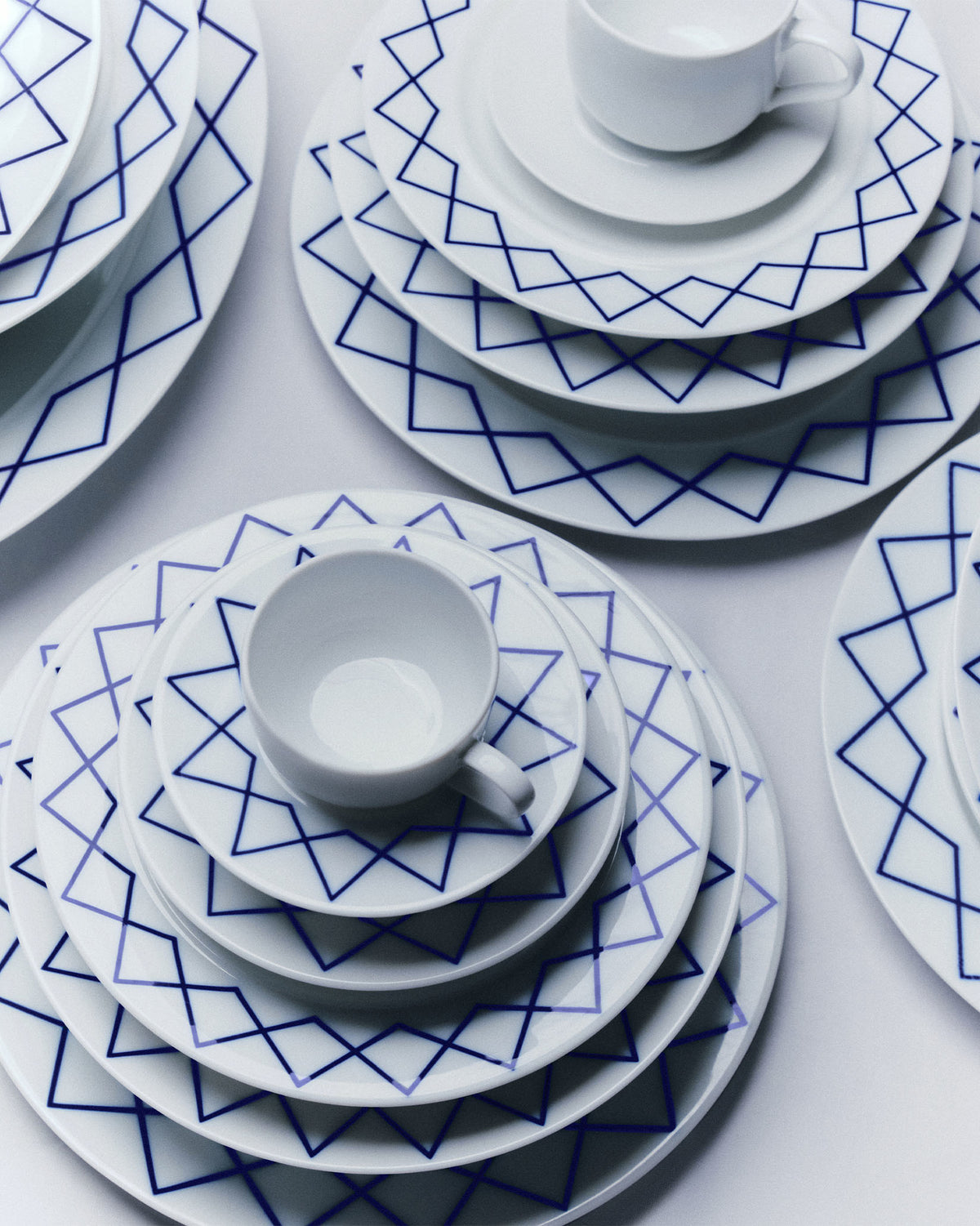 White china saucers by Alessi featuring a blue geometric diamond pattern, arranged in stacked place settings.
