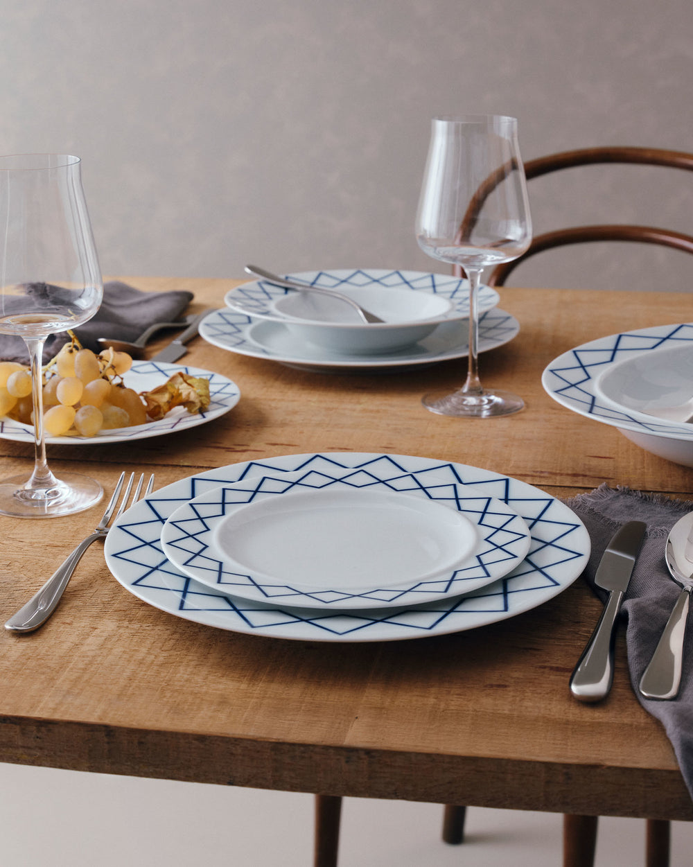 White ceramic soup bowls with blue geometric patterns by Alessi, part of a place setting on a wooden table.