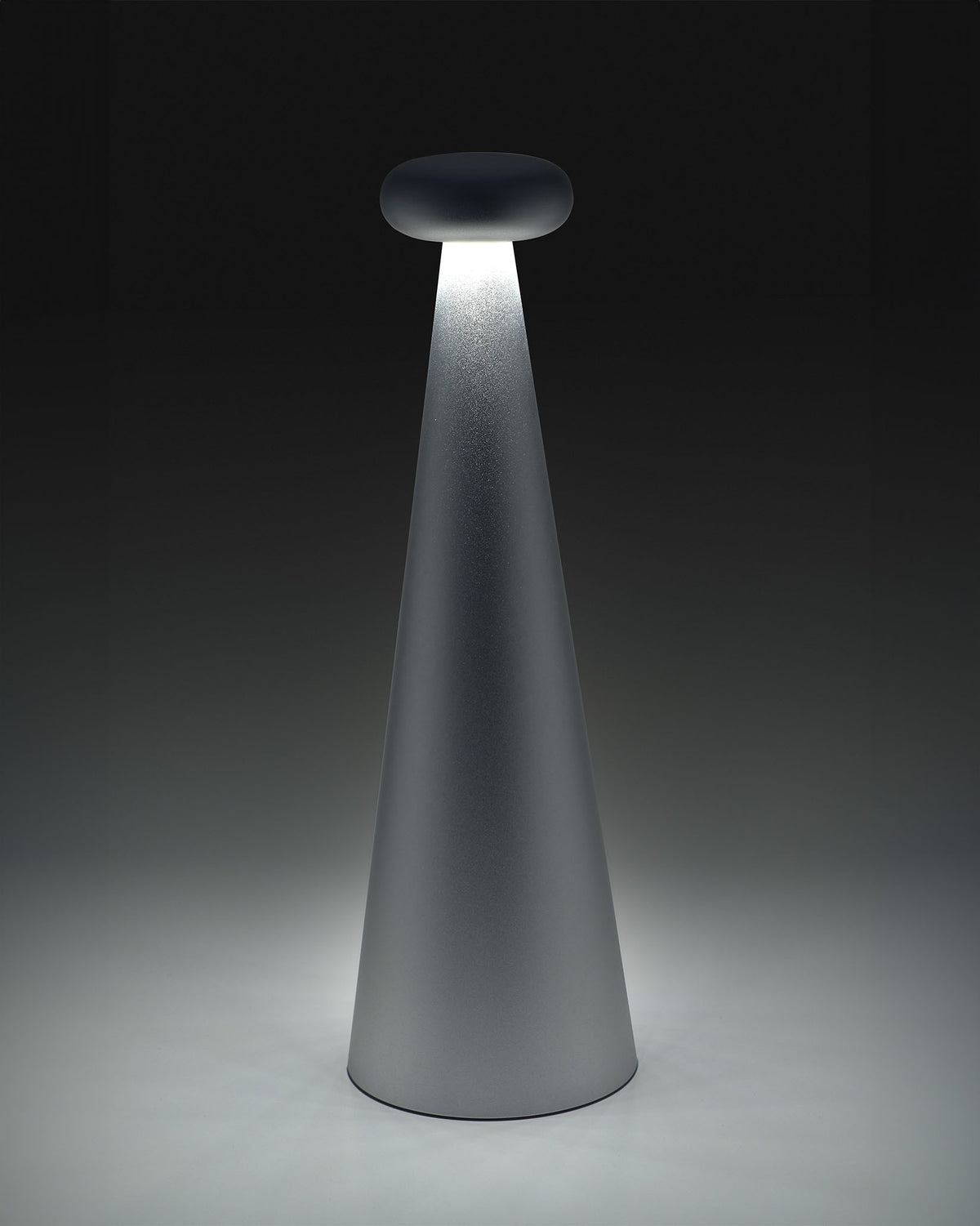 Gray conical Bedin lamp by Alessi, with a dark flat top emitting a bright downward light beam.