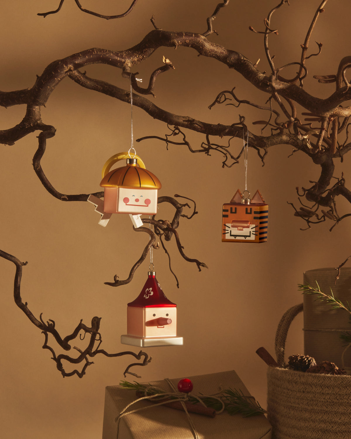 Geometric Quadrangelo Christmas tree ornaments by Alessi, depicting cheerful faces and a tiger, hanging from bare branches.