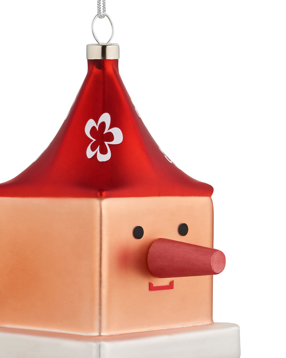 Red and peach cube-shaped Cubocchio Christmas tree ornament by Alessi with a conical hat, white flower, black eyes, long red nose, and red mouth.